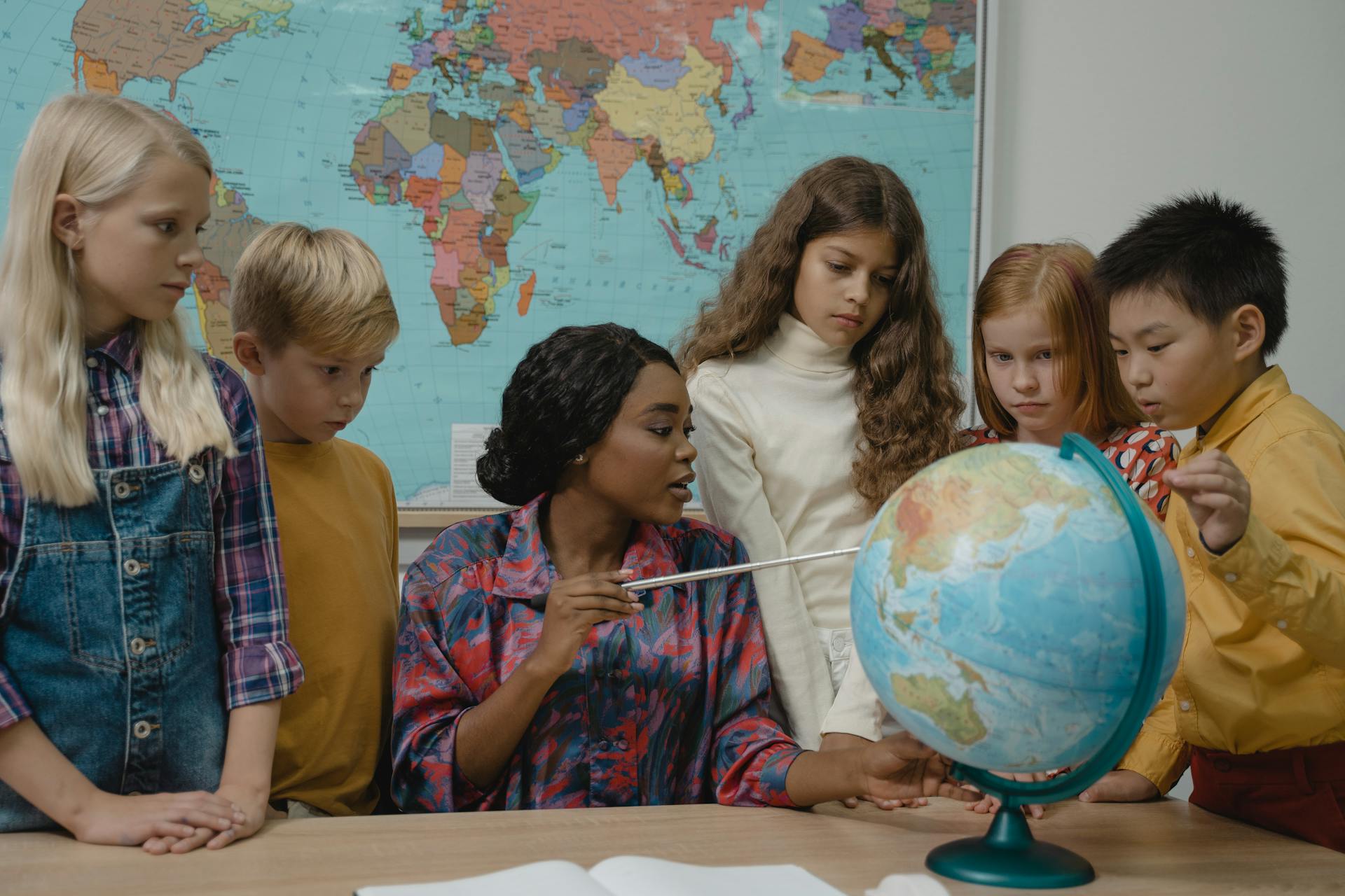 A teacher with diverse children gathered around a globe in a classroom